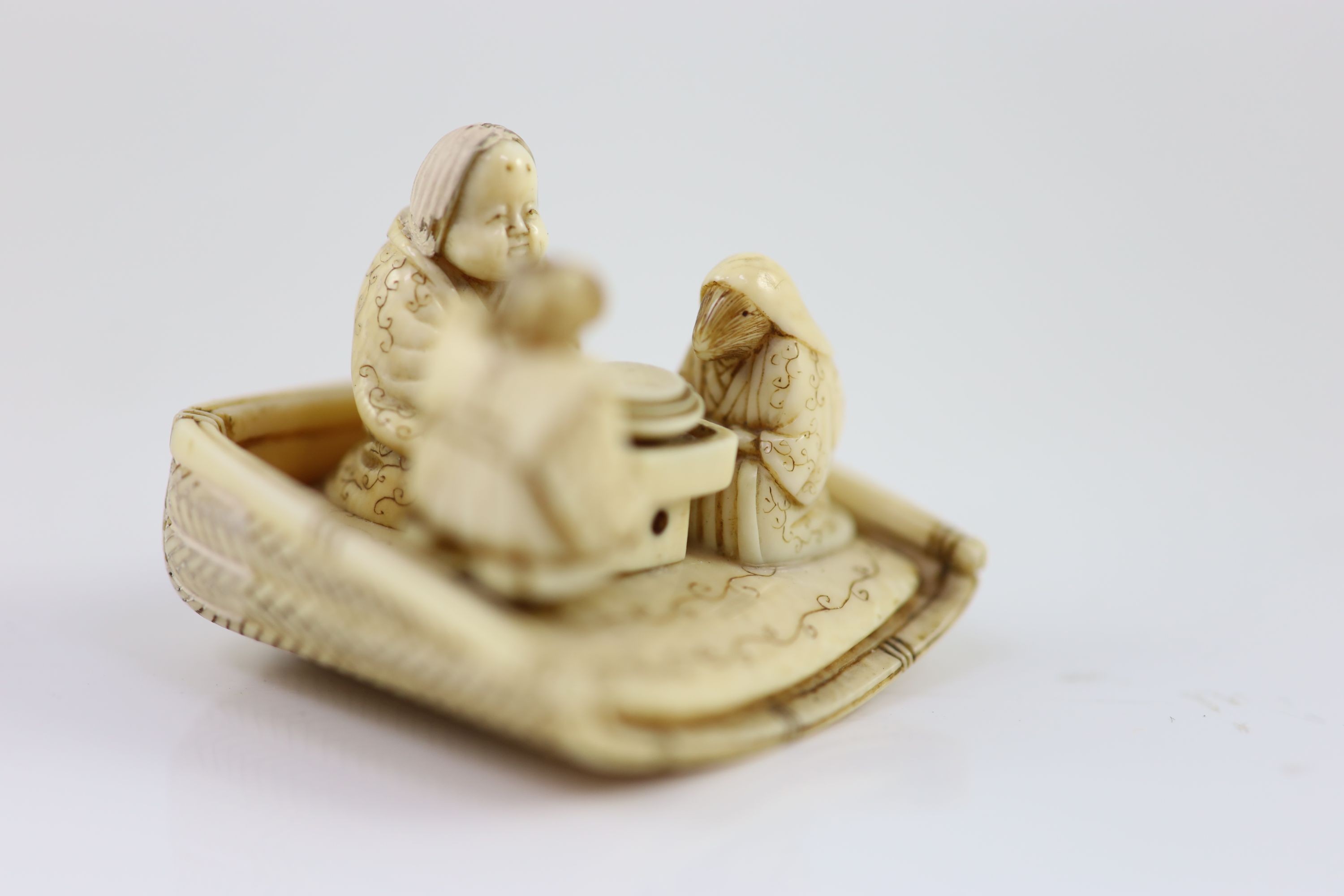 A Japanese ivory netsuke of figures seated around a table, Meiji period, 4.5 cm